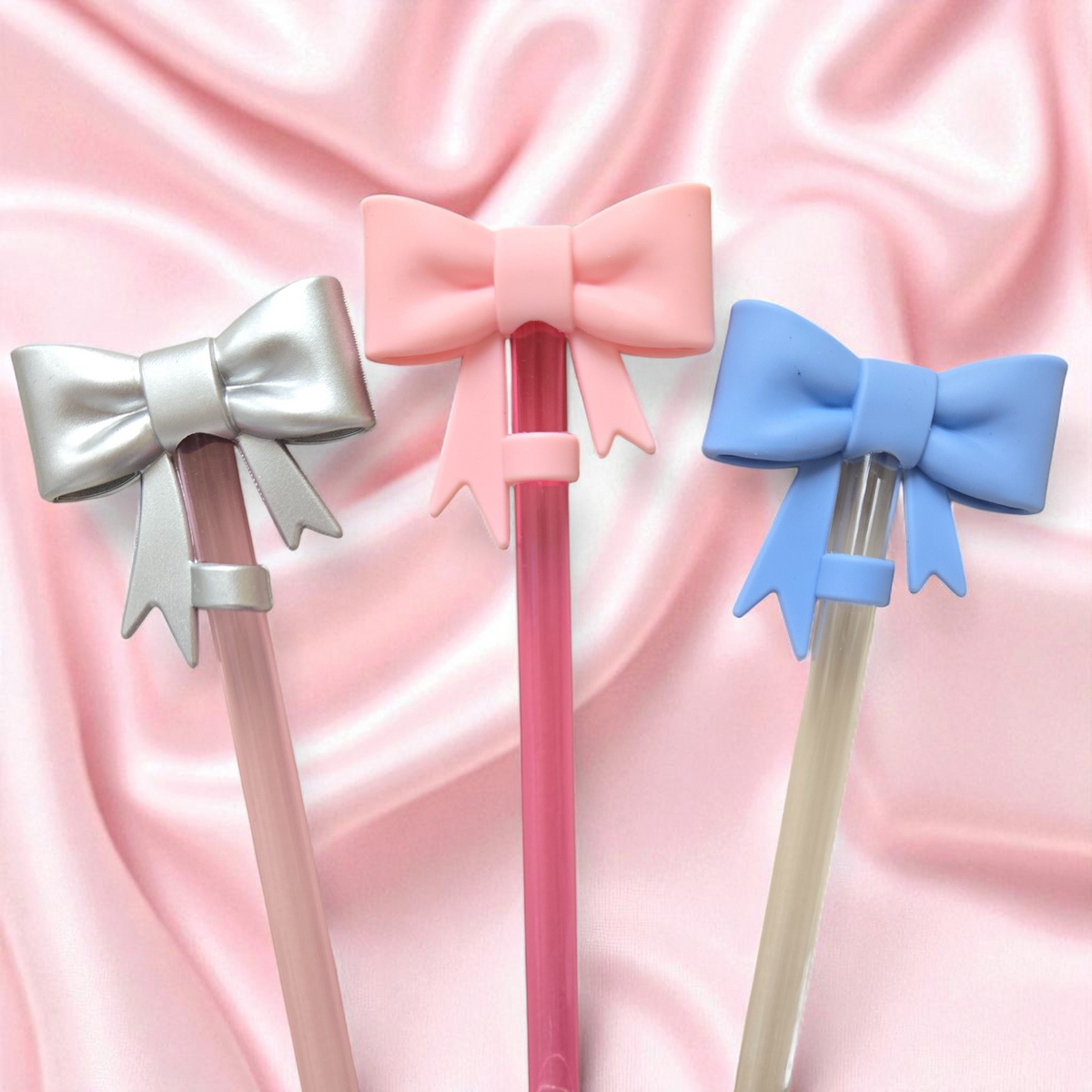 Biddlebee Three decorative straw topper bows on straws against a pink satin background