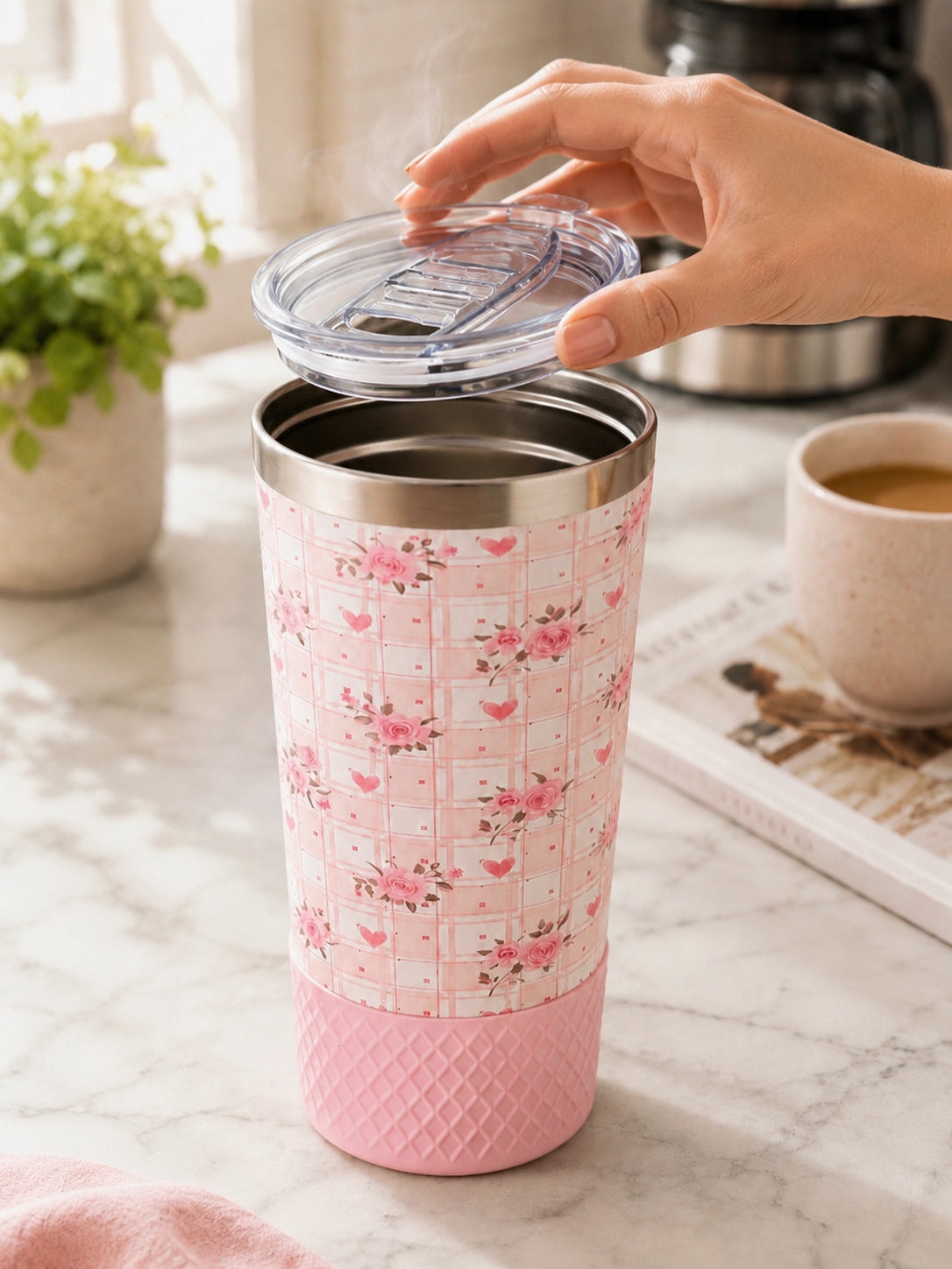 Hand placing the Biddlebee Brew coffee lid onto a Biddlebee 20oz Signature Collection tumbler in pink floral heart plaid print on a marble counter