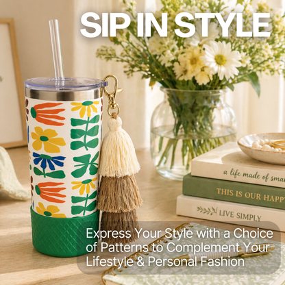 Biddlebee 20oz retro floral charm tumbler with green silicone boot, brown ombre tassel charm and easy sip straw lid  on a table with books and flowers, featuring text 'Sip in Style'.