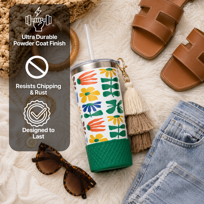 Biddlebee 20oz retro floral charm tumbler with green silicone boot, brown ombre tassel charm and easy sip straw lid  on a textured surface with sandals, sunglasses, and broom.