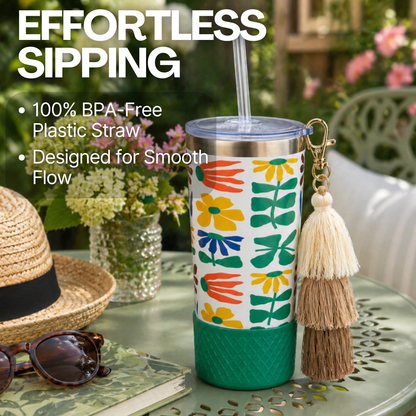 Biddlebee 20oz retro floral charm tumbler with green silicone boot, brown ombre tassel charm and easy sip straw lid on a patio table in a spring garden
