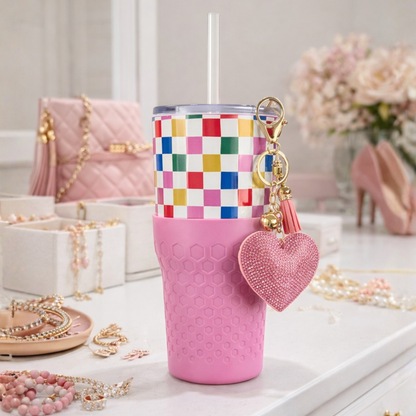 Biddlebee 30oz Happy Check Charm tumbler with easy sip straw, shimmer heart charm and silicone boot on a surface with jewelry and a handbag in the background.