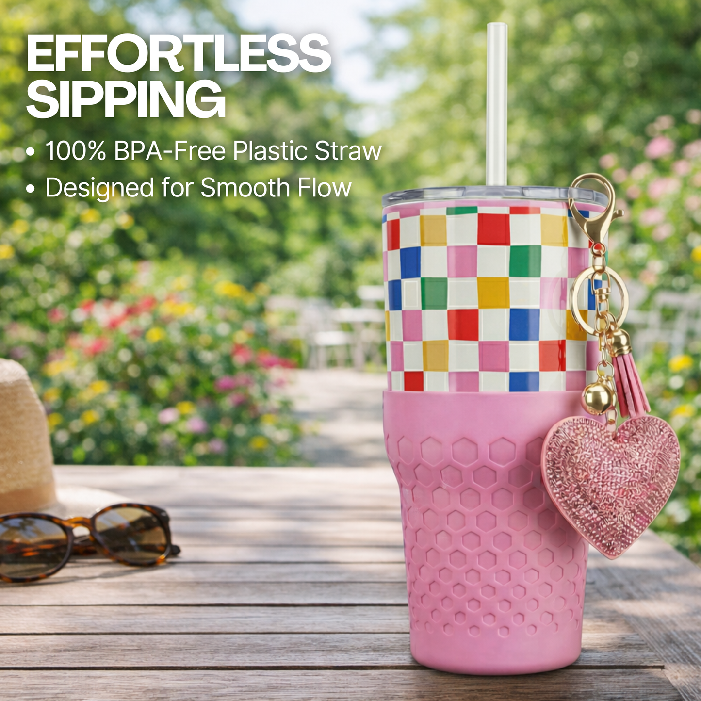 Biddlebee 30oz Happy Check Charm tumbler with easy sip straw, shimmer heart charm and silicone boot on a wooden surface with sunglasses and a straw, set against a blurred garden background.