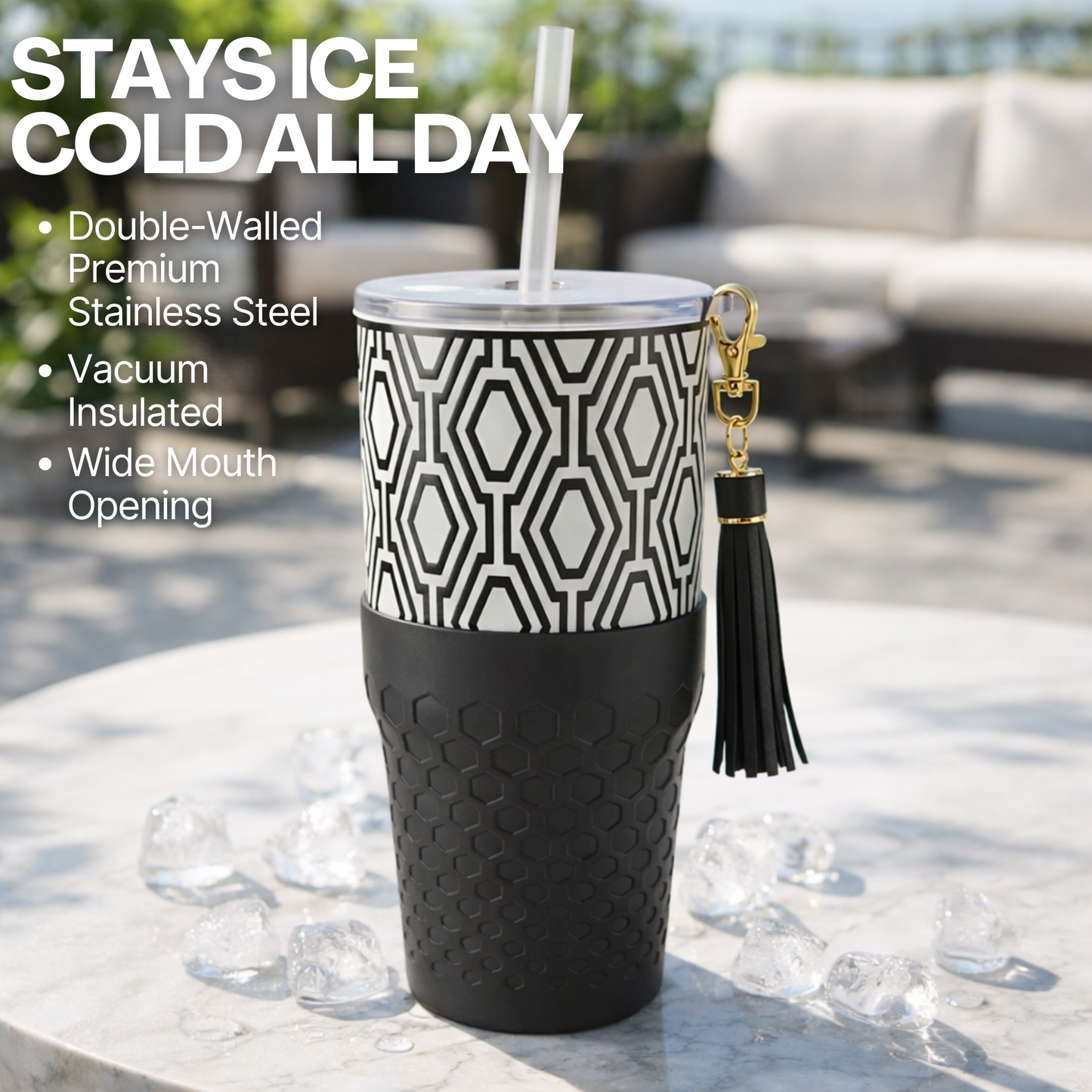Biddlebee 30oz Black & White Charm tumbler with a straw lid, vegan tassel and silicone boot on a white background on a table outdoors.
