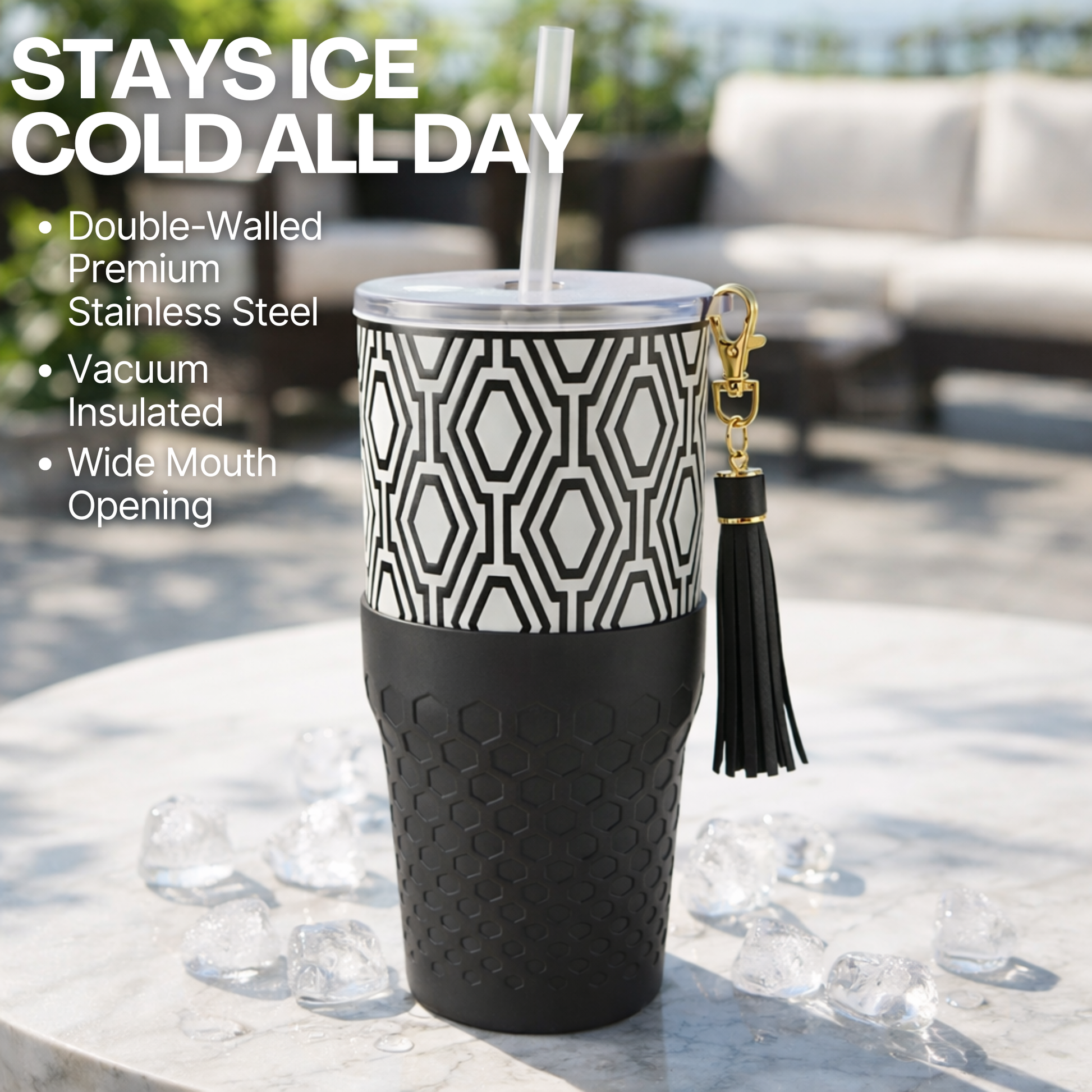 Biddlebee 30oz Black & White Charm tumbler with a straw lid, vegan tassel and silicone boot on a white background on a table outdoors.