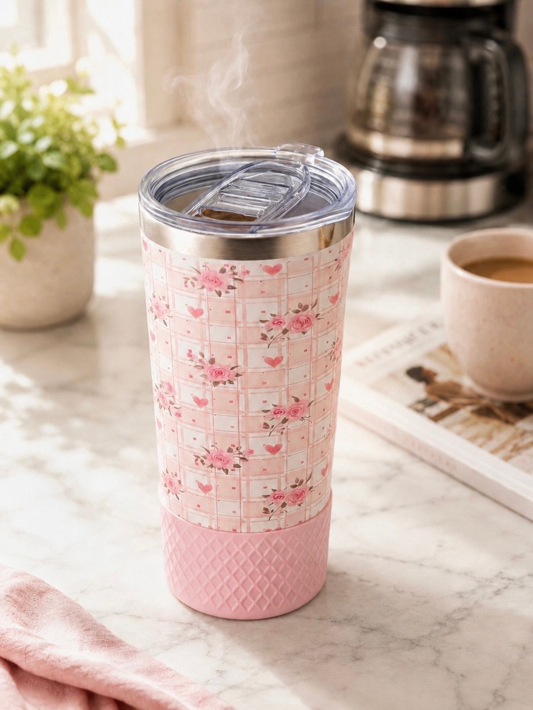 Biddlebee 20oz Signature Collection tumbler in pink floral heart plaid print with pink silicone boot and Biddlebee Brew coffee lid, styled on a marble kitchen counter next to a coffee maker