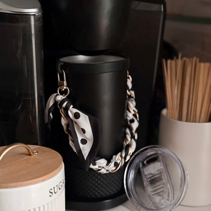 Biddlebee Brew Black coffee tumbler  with a decorative chain draped over it, surrounded by coffee-making equipment.