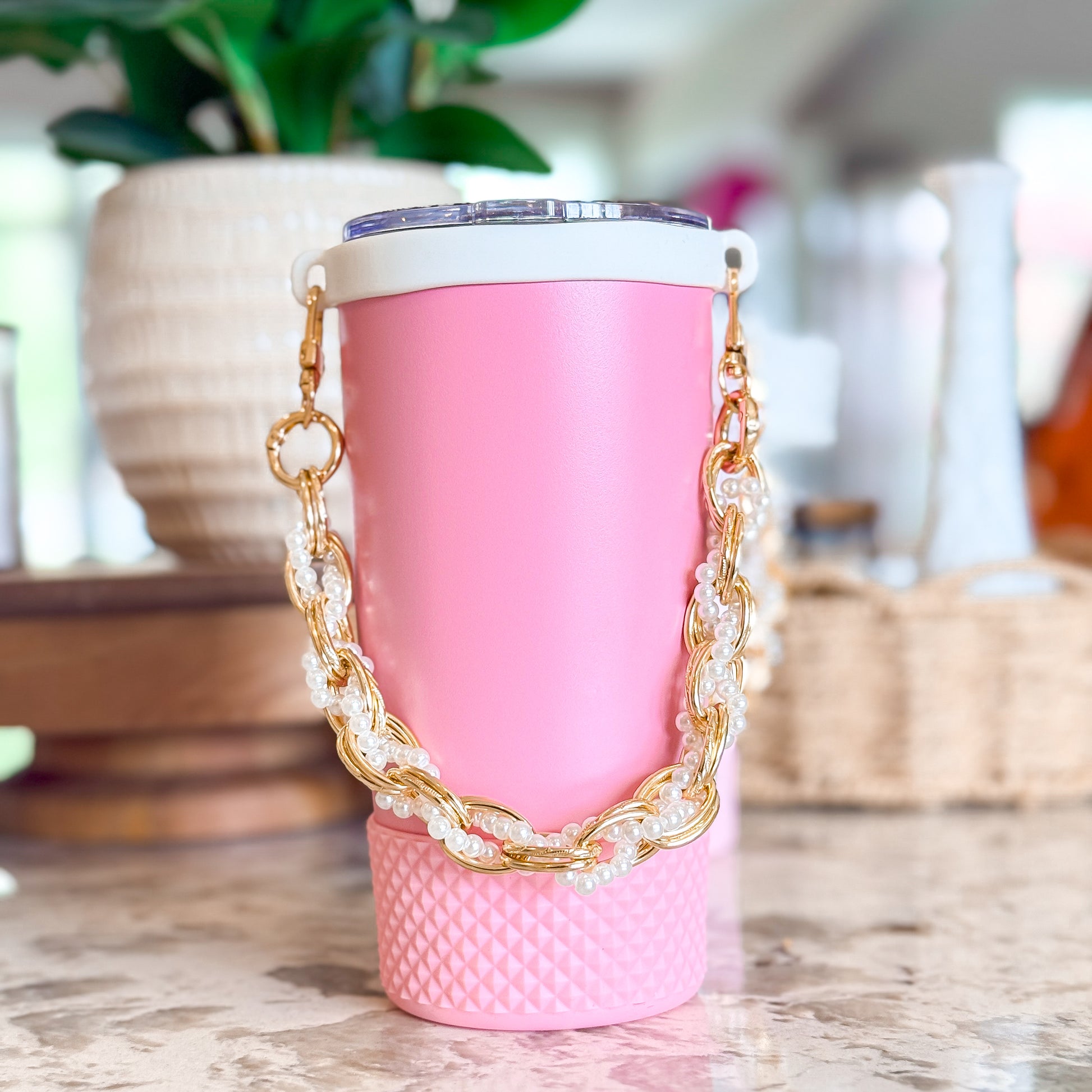 Biddlebee Brew Pink Tumbler with a gold chain handle on a wooden surface