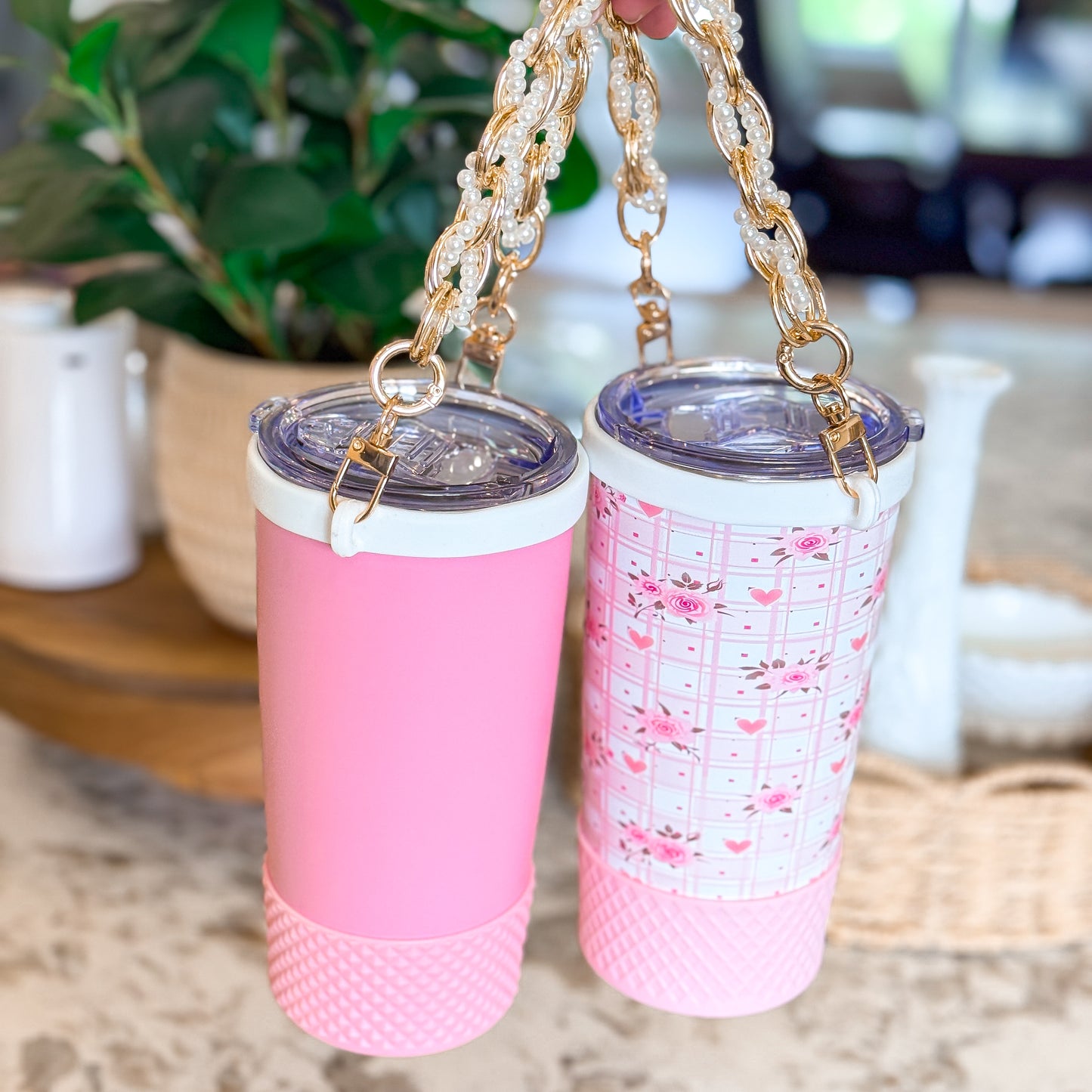Two Biddlebee Brew Pink Tumblers with floral pattern and plain design on a surface with a blurred background.