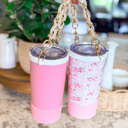 Two Biddlebee Brew Pink Tumblers with floral pattern and plain design on a surface with a blurred background.