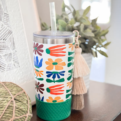 Biddlebee 20oz retro floral charm tumbler with green silicone boot, brown ombre tassel charm and easy sip straw lid  on a surface with decorative items.